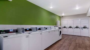 A modern laundry facility with multiple washing machines and dryers, green walls, and a wooden floor.