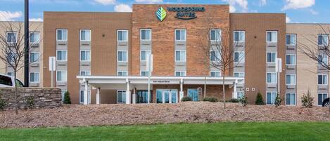 A hotel with a brick facade, a sign reading "Woodspring Suites," and a covered entrance.