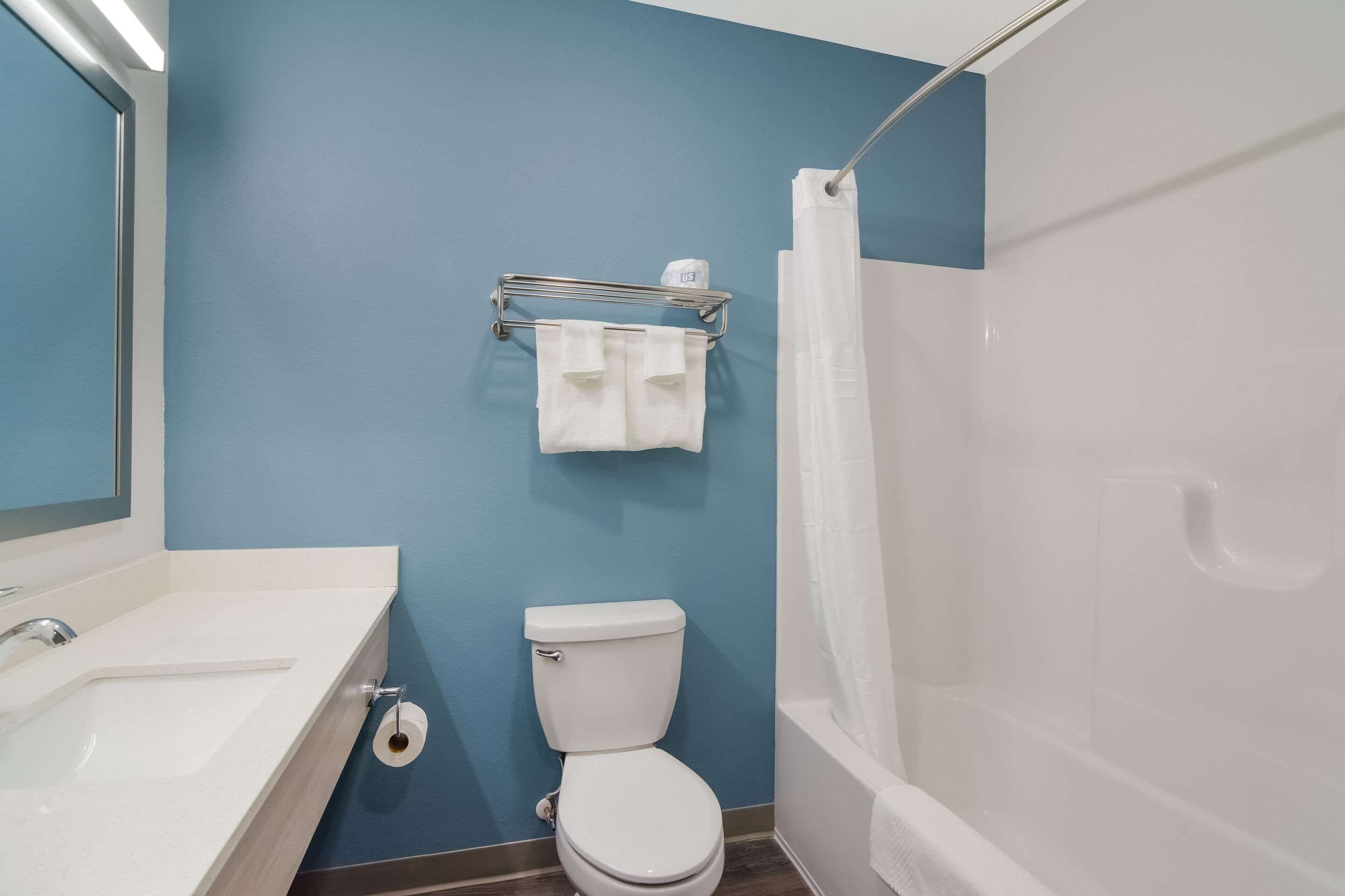 A bathroom with a white sink, toilet, and shower. There is a towel rack with two towels and a toilet paper roll.