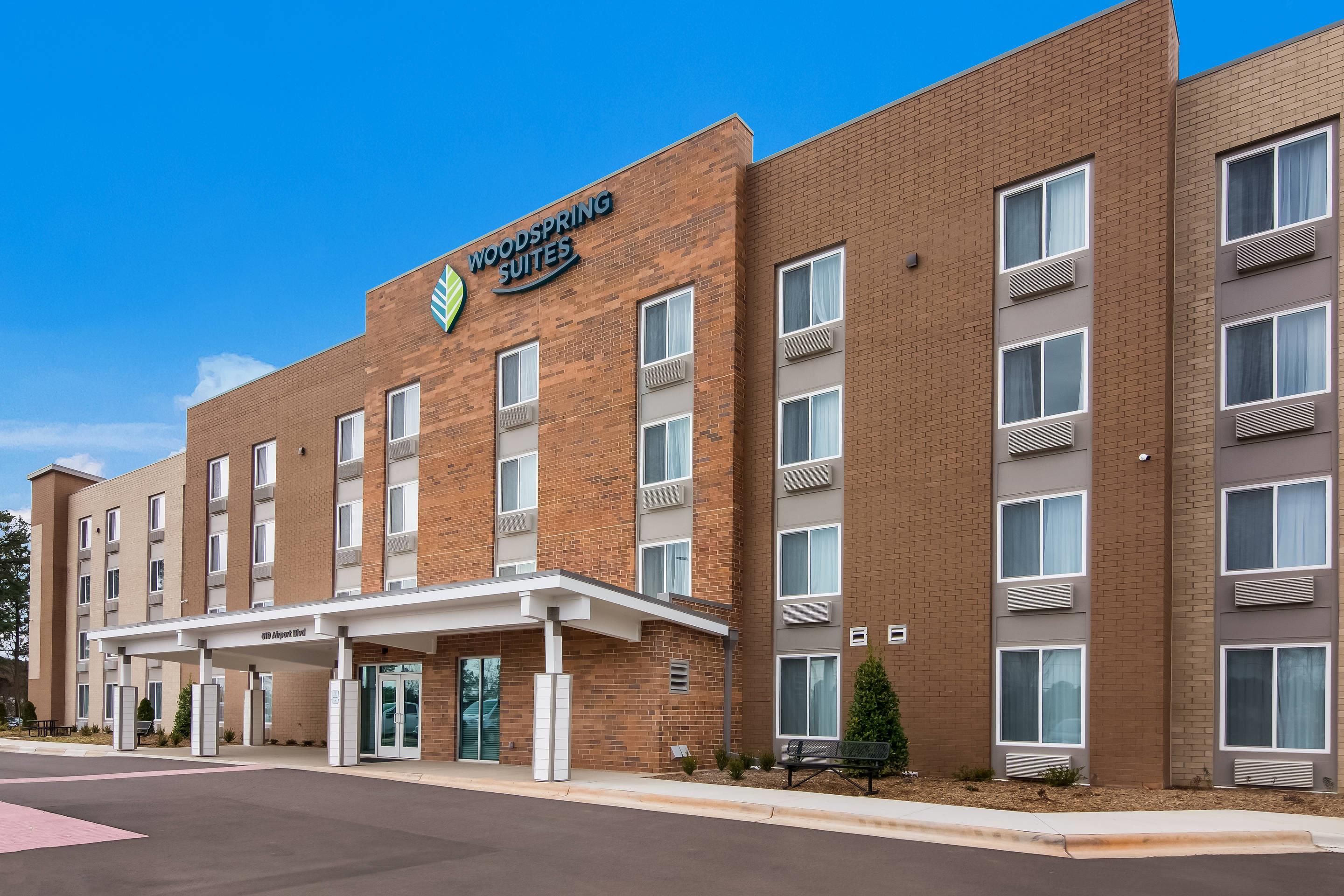 A multi-story hotel with a brick facade, a covered entrance, and a sign reading 'Woodspring Suites.'