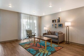 A modern living room with a sofa, a chair, a coffee table, a floor lamp, and a rug. - WoodSpring Suites Morrisville Raleigh Durham Airport (Morrisville)