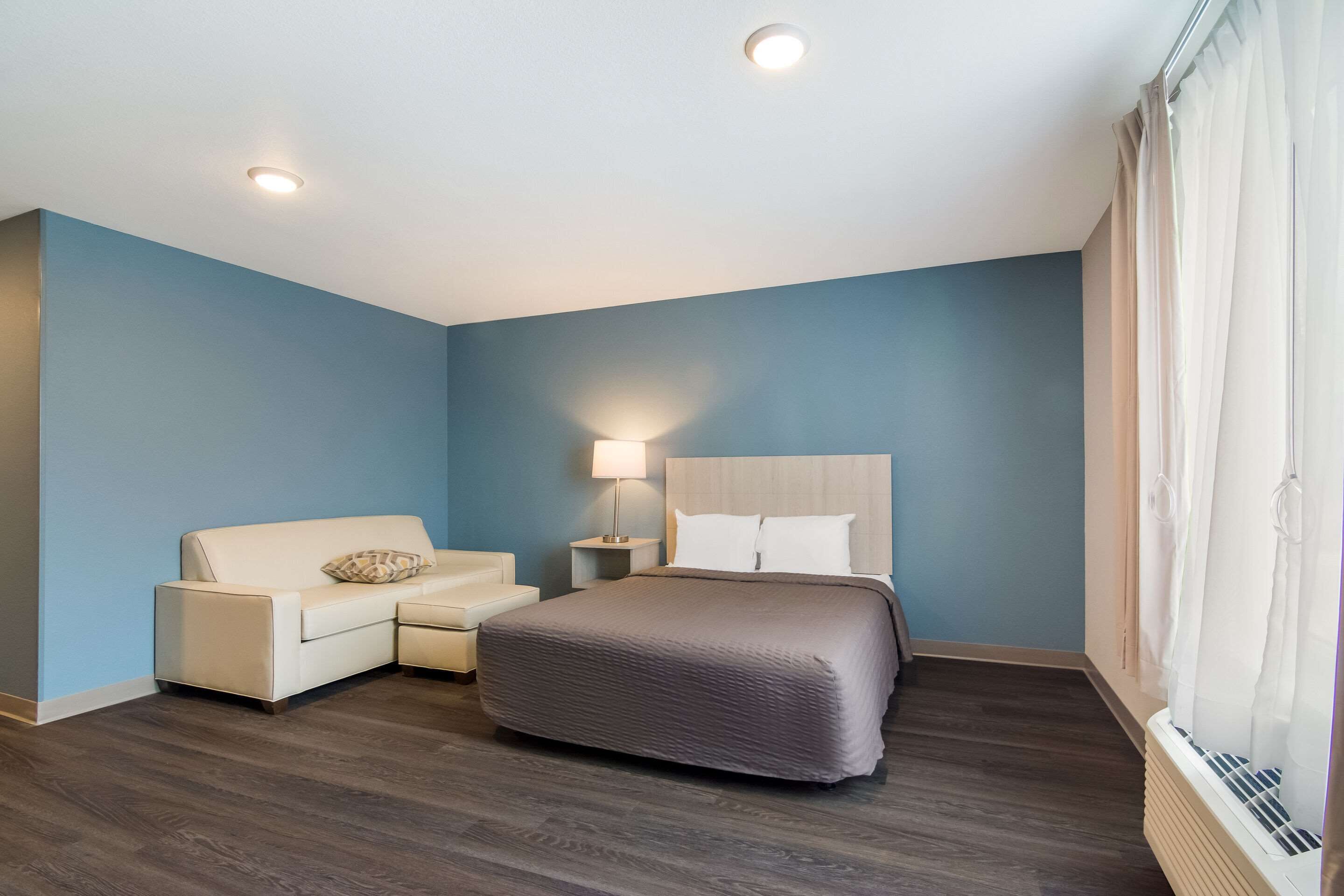 Una habitación de hotel con cama, sofá, mesita de noche y lámpara.