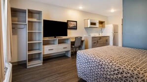 A compact hotel room with a bed, a desk, a chair, a TV, a microwave, and a refrigerator. - WoodSpring Suites Knoxville West (Knoxville)