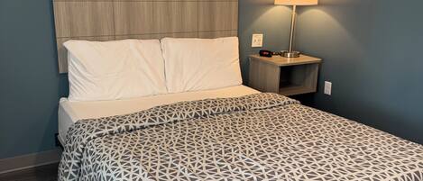 Una cama bien hecha con una colcha de estampado geométrico, un cabecero de madera y una mesita de noche con una lámpara.