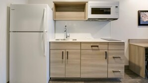A compact kitchen with a white refrigerator, a microwave, and wooden cabinets. - WoodSpring Suites Knoxville West (Knoxville)