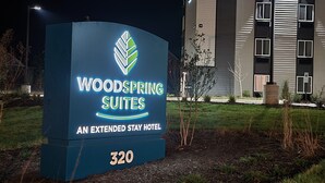 A sign for Woodspring Suites, an extended stay hotel, with a modern building in the background. - WoodSpring Suites Knoxville West (Knoxville)