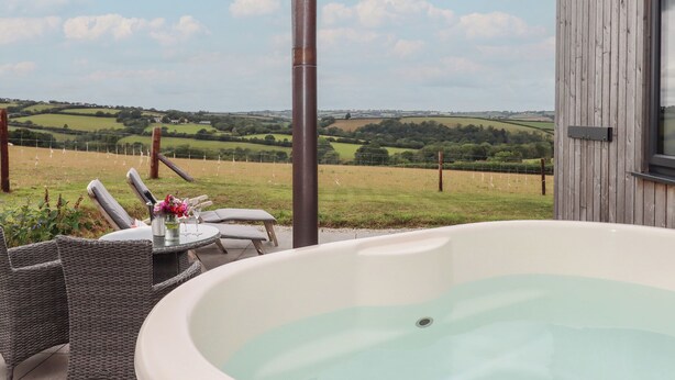 A hot tub with a view of rolling hills and a wooden building. - The Pennymoor (Tiverton)