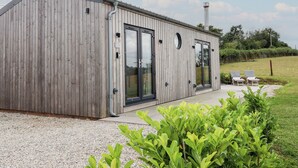 A modern wooden building with large glass doors and windows, a chimney, and a small outdoor seating area with two chairs. - The Pennymoor (Tiverton)