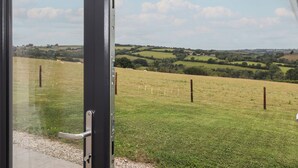 A view through a glass door of a rural landscape with rolling hills and a clear sky. - The Pennymoor (Tiverton)