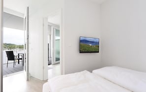 Ein Schlafzimmer mit Bett, Fernseher an der Wand und einem Balkon mit Stuhl.