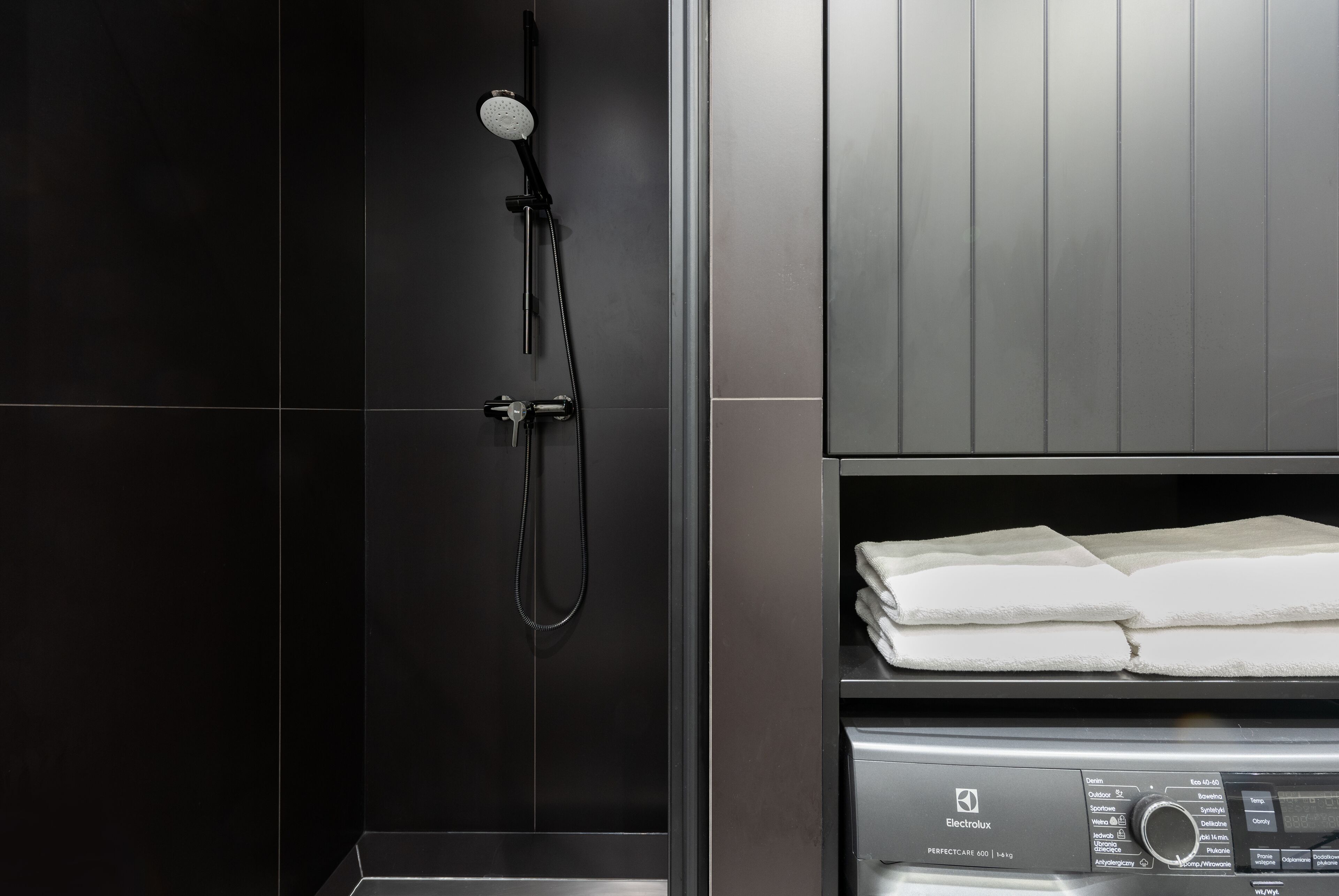 A modern bathroom with a black tiled wall, a shower with a handheld showerhead, and a control panel labeled "Electrolux PERFECTCARE 600".