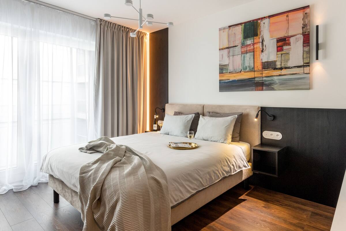 A modern bedroom with a large bed, a bedside table, a nightstand, and a wall-mounted artwork.