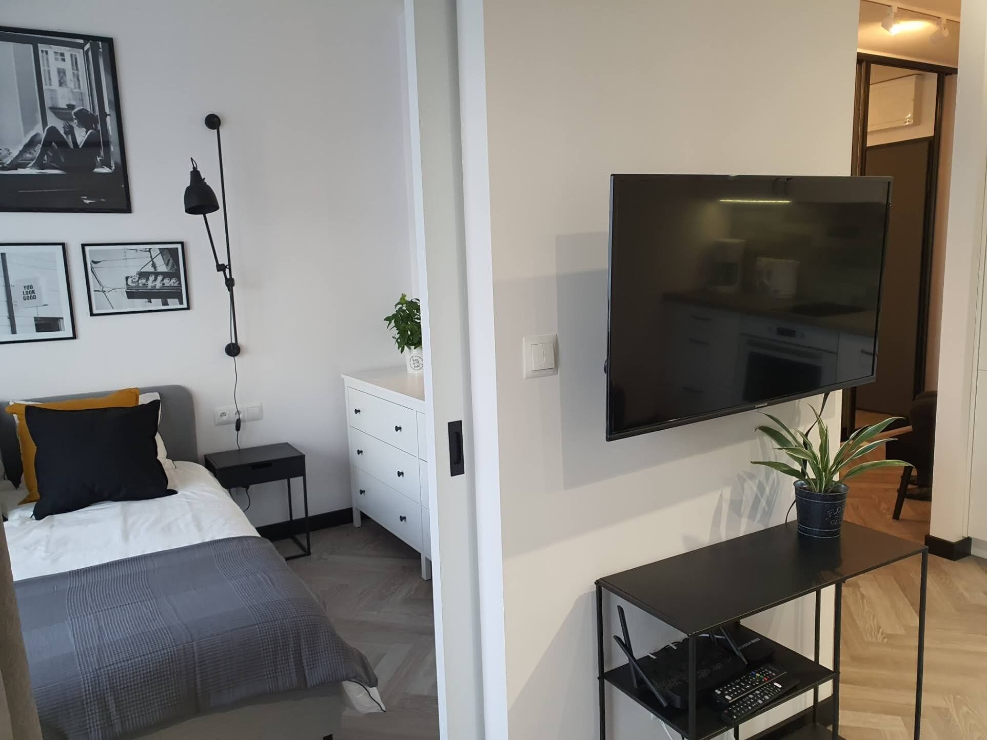 A modern bedroom with a bed, bedside tables, a TV, and a small desk with a plant.