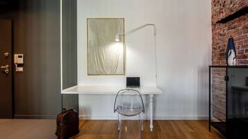 Una habitación moderna con un escritorio blanco, una silla transparente, una computadora portátil, una lámpara, una pared de ladrillo y suelo de madera.