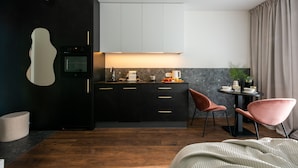 Una cucina moderna con mobili scuri, forno a incasso e zona pranzo con due sedie rosa e un tavolino.