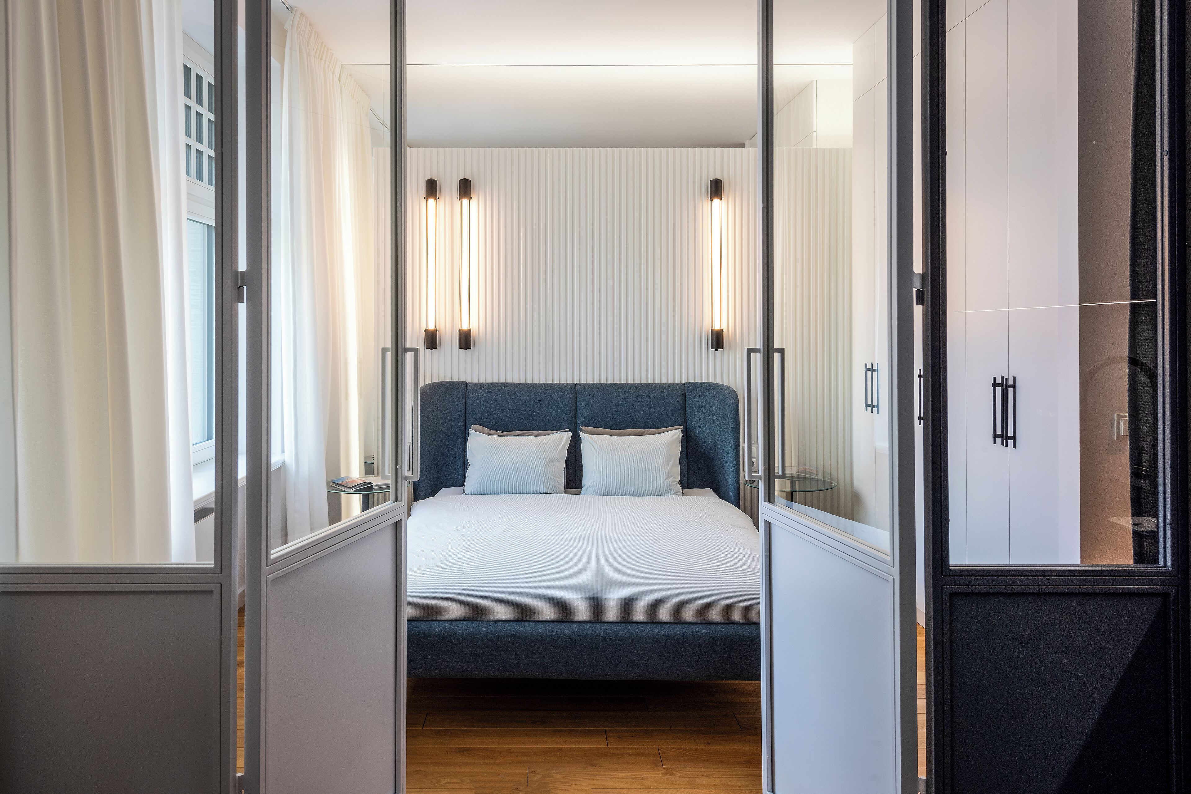 A modern bedroom with a bed, bedside tables, and a view through a glass door.