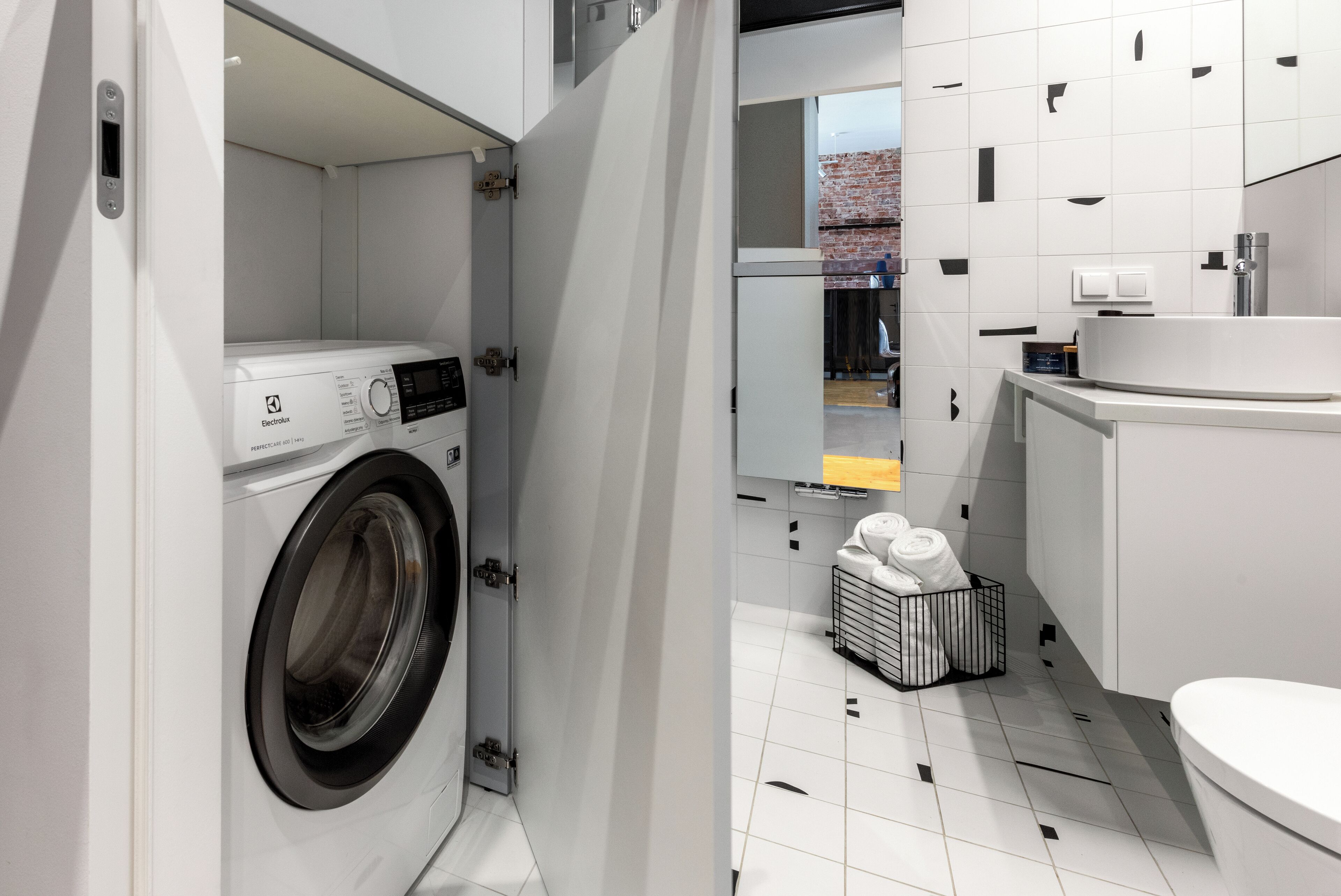 Een moderne wasruimte met een voorlader wasmachine, een klein wastafeltje en een toilet.