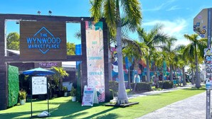 El Mercado Wynwood, con fachada de madera, césped artificial verde y palmeras.