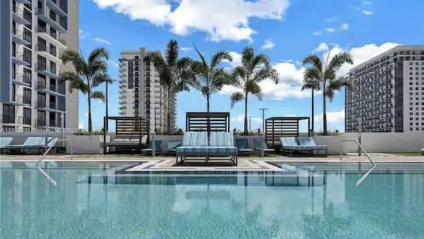 A swimming pool with lounge chairs and palm trees, surrounded by high-rise buildings.