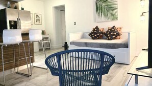 Ein modernes Wohnzimmer mit einem weißen Sofa, einem blauen Sessel und einem Essbereich mit weißen Stühlen.