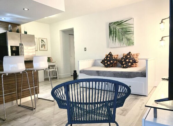 A modern living room with a white sofa, blue chair, and a dining area with white chairs.