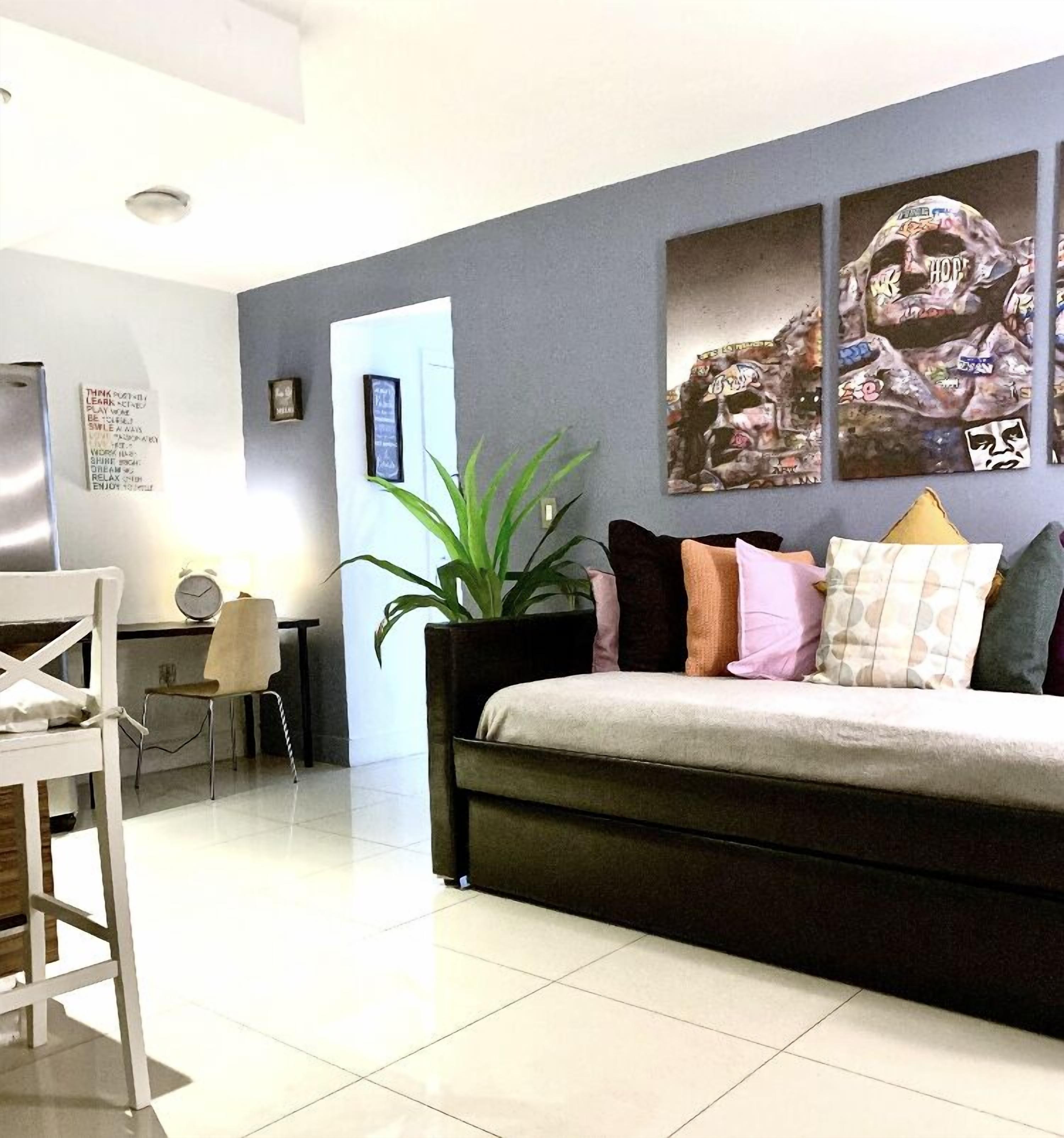 Een moderne woonkamer met een donkere bank, een eettafel met stoelen, een plant in pot en kunst aan de muren.