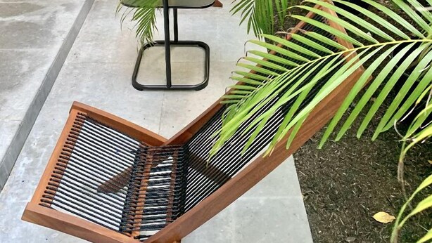 A modern outdoor seating area with a wooden chair and a small table, surrounded by lush green plants and a concrete floor. - THE GROVE 1  10 MIN FROM THE BEACH. In the heart of Coconut Grove. CocoWalk (Miami)