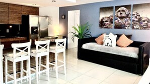 A modern living room with a black sofa, white chairs, and a dining area with a table and chairs. - THE GROVE 1  10 MIN FROM THE BEACH. In the heart of Coconut Grove. CocoWalk (Miami)
