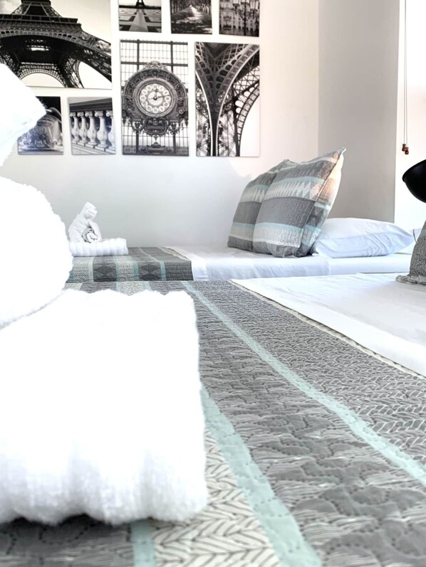 Un dormitorio con cama, almohadas y una alfombra. Hay decoraciones en la pared, incluyendo un reloj y una estructura que recuerda a la Torre Eiffel.