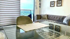 A modern living room with a glass table, a grey sofa, and a view of the outdoors through large windows. - A1608 AWESOME Downtown Doral Apartment (Doral)
