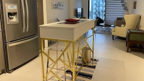 A modern kitchen with a stainless steel refrigerator, a small white table with a red bowl, and a yellow-legged stool. There is a dining area with a yellow chair and a small table. - A1608 AWESOME Downtown Doral Apartment (Doral)
