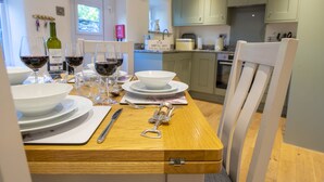 A dining table set with wine glasses, plates, and cutlery in a room with light-colored wooden furniture and green cabinets. - Witton View, Bellerby, Yorkshire Dales (Leyburn)