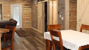Un interior rústico de madera con una mesa de comedor preparada para dos personas, paredes de madera y un techo con iluminación empotrada.