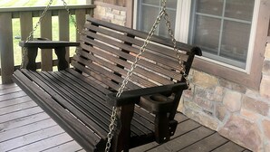Una mecedora de madera con cadenas de metal, un muro de piedra y una ventana.