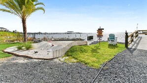A coastal walkway with a palm tree, a wooden fence, a signpost, and a chair by the water. - Pelican Pier Beach House on Lake Catherine (New Orleans)
