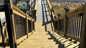 A wooden pier leading to a small covered structure over water, with a railing on both sides and a view of the water and distant land. - Pelican Pier Beach House on Lake Catherine (New Orleans)