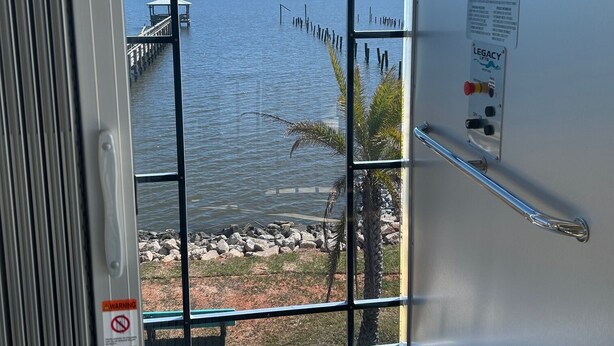 A view from a window with a metal railing, a warning sign, and a palm tree visible outside. - Pelican Pier Beach House on Lake Catherine (New Orleans)