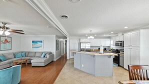 A modern kitchen with white cabinets, a central island, and a dining area with a wooden table and chairs. - Pelican Pier Beach House on Lake Catherine (New Orleans)
