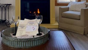 A living room with a fireplace, a television mounted above it, and a comfortable seating area with a sofa and a small table with glasses and papers.