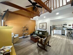 A spacious living room with a high ceiling, a staircase, a kitchen area, and a dining space.