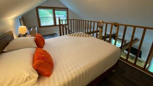 A bedroom with a large bed, a wooden railing, and a window with a view.