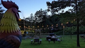 A grassy outdoor area with string lights, a wooden structure, and tables and chairs set up for an event.