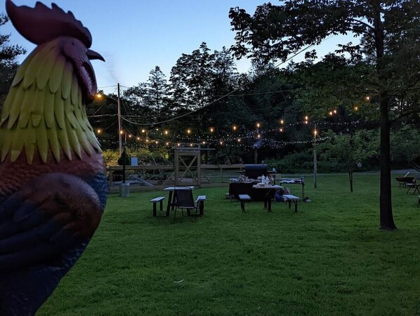 A grassy outdoor area with string lights, a wooden structure, and tables and chairs set up for an event. - New! Romantic Agrihood Bungalow Getaway-Fireplace/WiFi (Hurleyville)