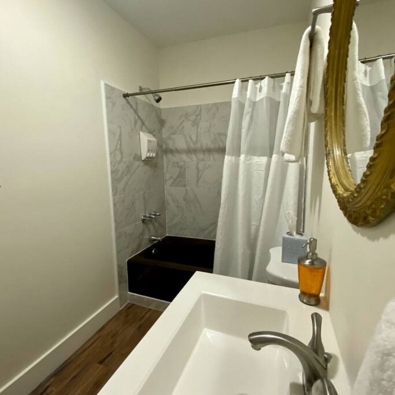 Un baño con lavamanos blanco, ducha con puerta de cristal y pared de mármol.