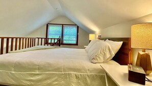 Une chambre à coucher avec un grand lit, une table de chevet, une lampe et une vue sur l’extérieur par une fenêtre.