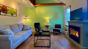 Un salon avec un mur vert, une cheminée, un canapé, deux fauteuils, une table basse et un tableau.