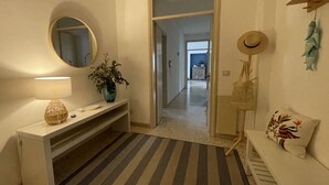A hallway with a striped rug, a round mirror, a vase with flowers, a lamp, a hat on a stand, and a colorful pillow on a bench. - Elegant and bright apartment with terrace on the waterfront of Aci Trezza (Aci Trezza)