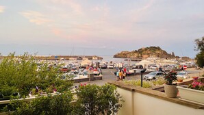 A marina with boats docked, a rocky island in the background, and people walking. - Elegant and bright apartment with terrace on the waterfront of Aci Trezza (Aci Trezza)