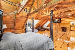 Cozy attic-style bedroom with a sloped ceiling, featuring a large bed and wall-mounted TV.