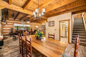 Cozy cabin-style room with a dining table, comfortable seating area, and staircase leading to an upper level.